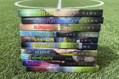 A stack of ten romance novels by Amy Daws, titled Sweeper, Replay, Blindsided, Payback, Dominate, Surrender, Keeper, Endurance, Challenge, and Strength, displayed on a wooden shelf.